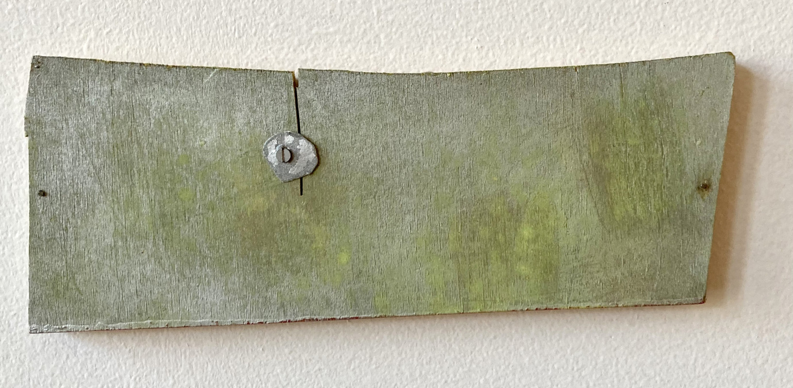 This weathered wooden wall plaque features a distinct green patina and a metallic decorative element fastened to the center.