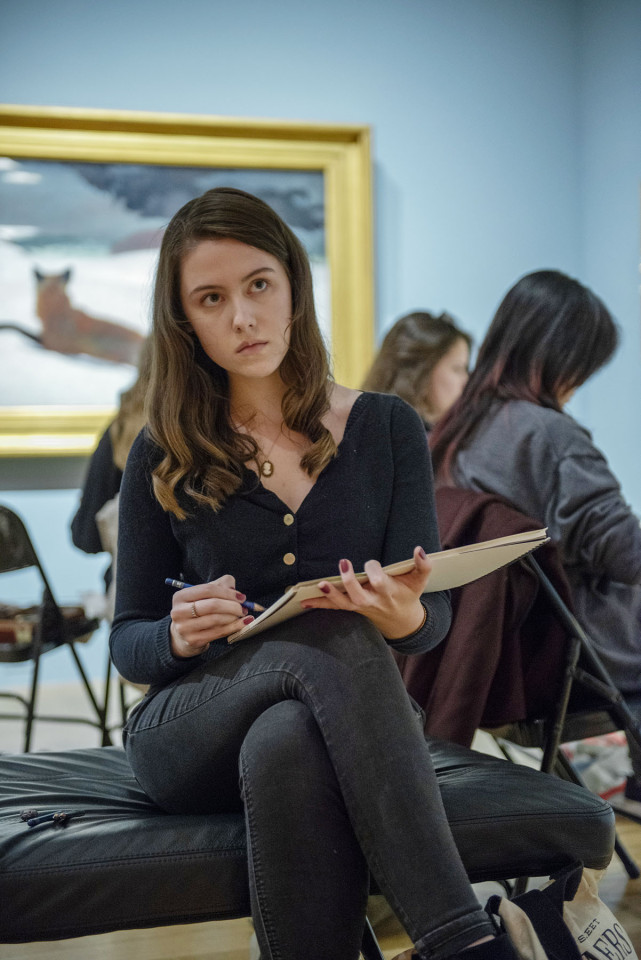 student sketching in gallery with painting behind