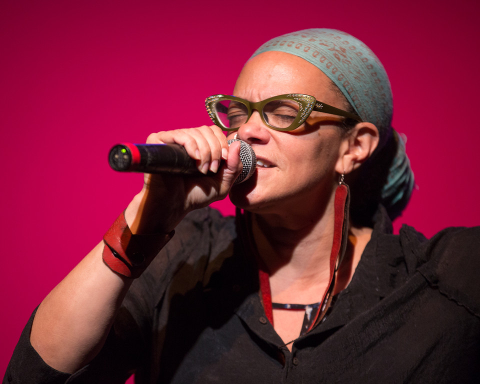 Photo of Ursula Rucker performing with a pink background. 