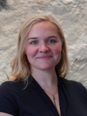 Bio photo of Kelin Baldridge Smallwood who is light skinned, and has shoulder length blond hair. Kelin is smiling lightly and wearing a black blouse. 