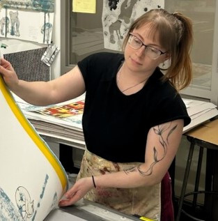 Photo of Justine Ditto, a light-skinned woman with sandy-colored hair pulled back in a ponytail, pulling a print from a litho press