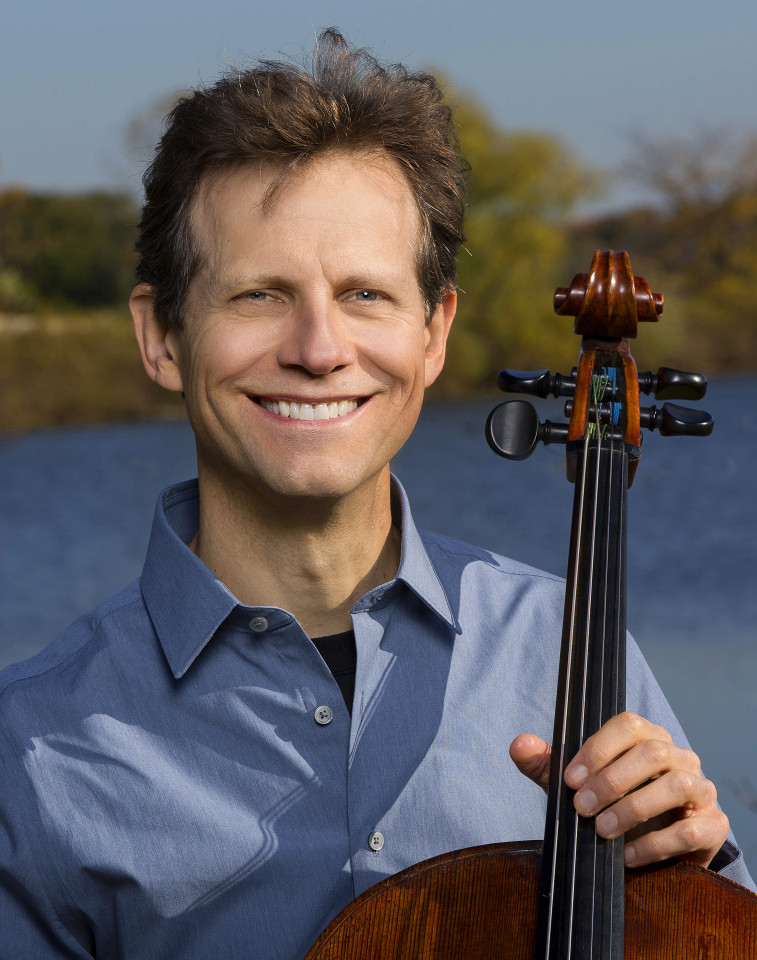 bio photo of Bob Cafaro who is light skinned with short brown wavy hair, holding the neck of a cello. Bob is posing outdoors with a lake in the background. 