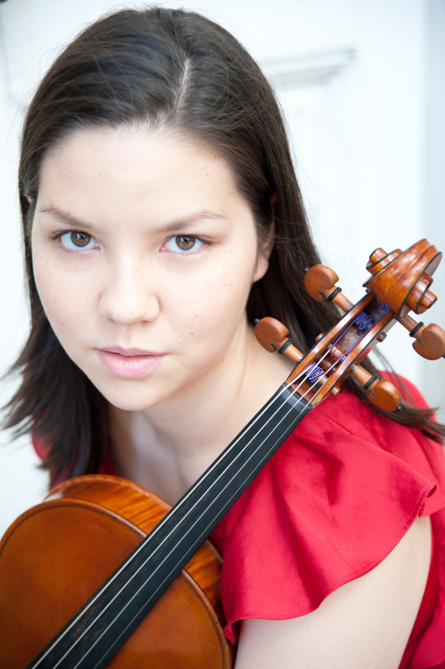 Bio photo of Ren Martin-Deiko taken from above. Ren is fair-skinned with dark straight hair parted on the left side. Ren is wearing a red dress with short ruffled sleeves. A violin is resting on Ren's left shoulder. 