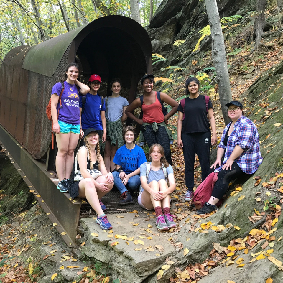group of students posing in front of a tunnel in the woods
