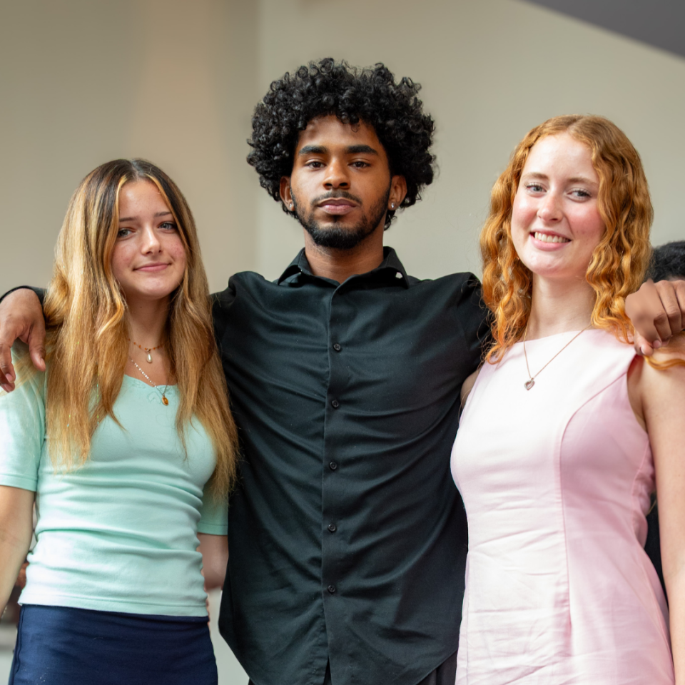 three young people posing together indoors against a neutral background.