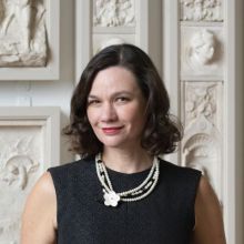 Bio photo of Dr. Anna O. Marley. Anna is a light-skinned person with dark, shoulder-length hear. Anna is wearing red lipstick, and sleeveless black dress and a beaded black and white necklace. 