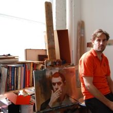 person sitting against table with their artwork and tools around them