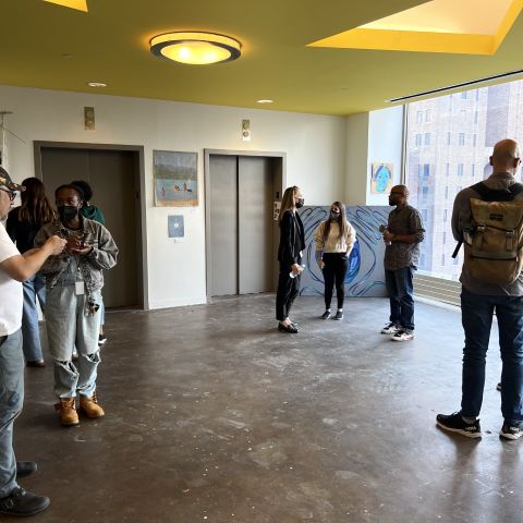 students standing and eating in open gallery area with elevators and large window behind