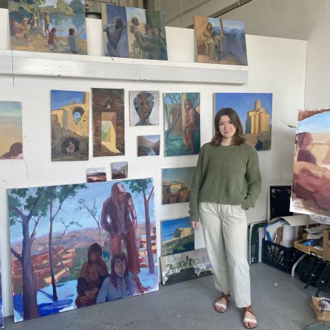 Anna Hoppel in her studio posing with her paintings.