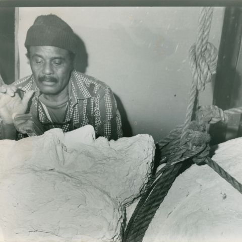 Black and white photograph of a Black man wearing a hat working on a sculpture of Frederick Douglass