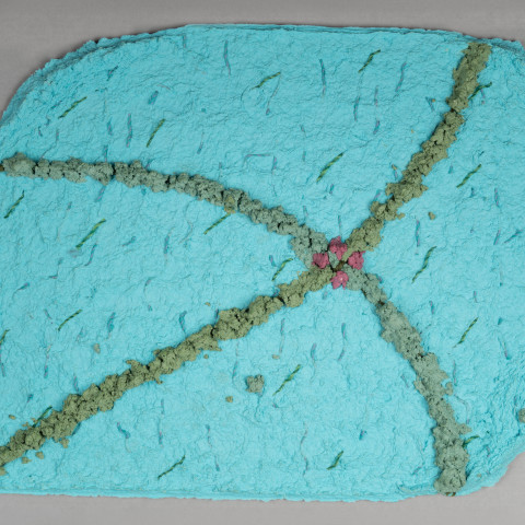 A textured turquoise handmade paper artwork features intersecting grayish-green fibrous lines that meet at a central cluster of small pink floral shapes.