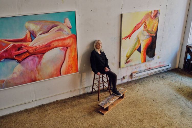 Joan Semmel sits in studio between two paintings