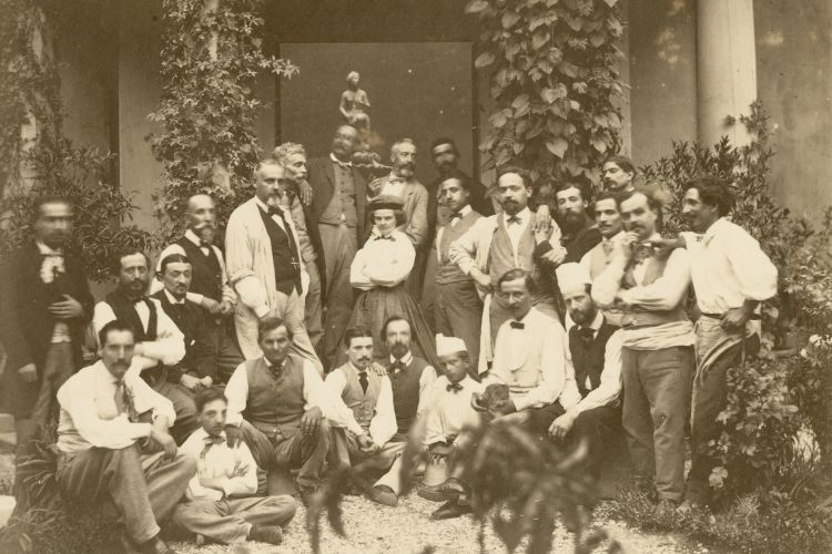 Black and white image of a large group of people in the late 1800s. Mostly men surrounding one woman who stands strongly with her arms crossed and wears a sly smile. The woman is Harriet Hosmer, she is wearing a white blouse and long full skirt. She is the aritst and all the men are her workmen in her studio. 
