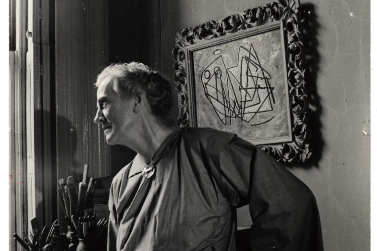 Black and white photo of Anne Ryan in her New York Studio looking out a window. 