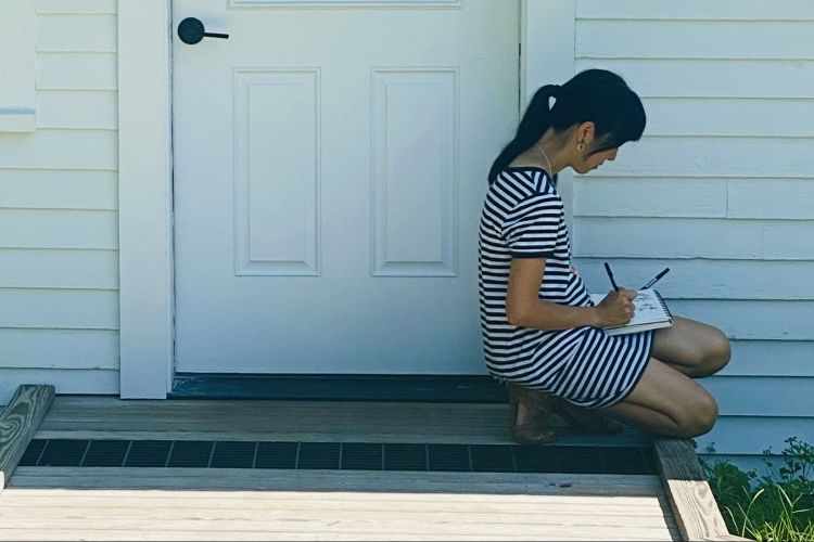 Woman sits on stoop in front of white wooden door