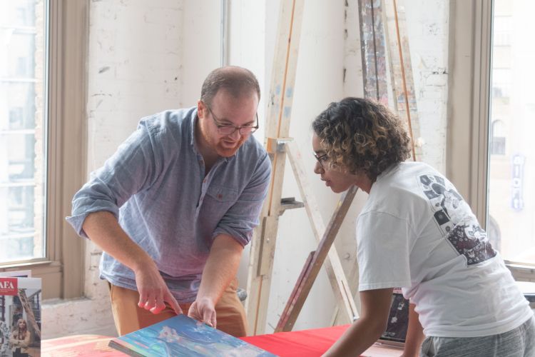 two people looking at painting over table with red tablecloth with pafa logo