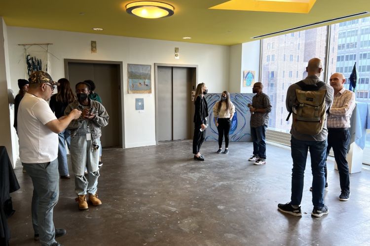students standing and eating in open gallery area with elevators and large window behind