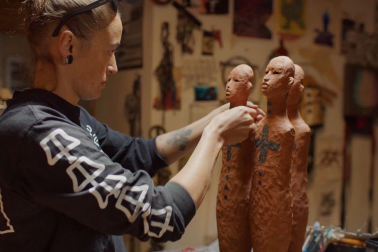 Artist in her studio working on three clay figures, each about 16 inches tall. 