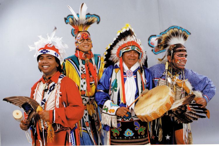 Studio portrait of four members of Thunderbird American Indian Dancers dressed in full regalia for performance