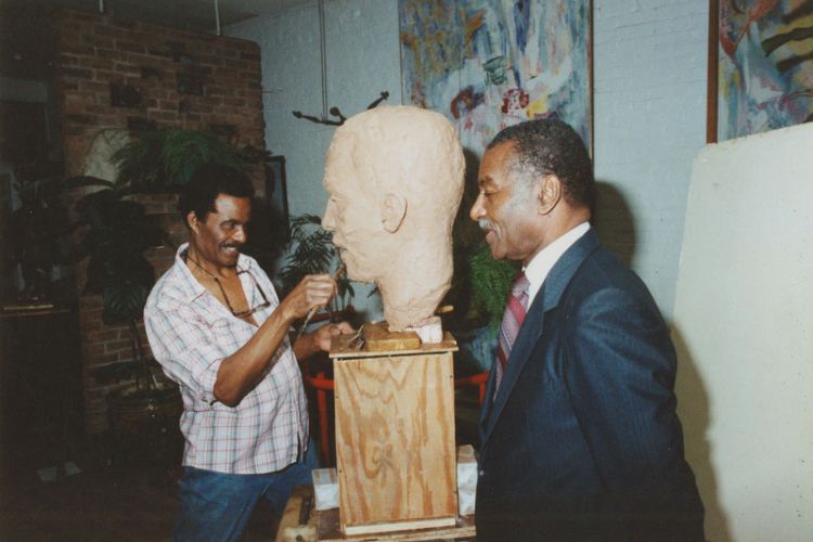 Color photograph of Fred Shuttlesworth modeling for John Rhoden during a sculpting session for the Birmingham Civil Rights Institute commission at Rhoden's home at 23 Cranberry Street in Brooklyn, N.Y.