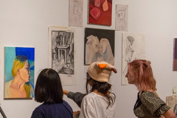 Three teenaged students examining the artwork of a peer