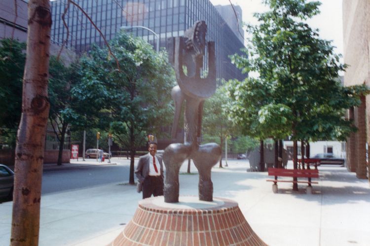 Color photograph of John Rhoden posing by a public art sculpture in front of the entrance to the African American Museum in Philadelphia.