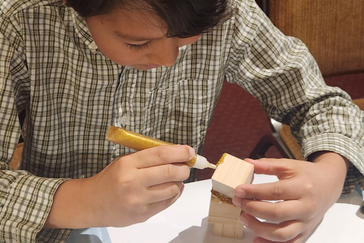 This image shows a child crafting with small wooden blocks and gold-colored glue.