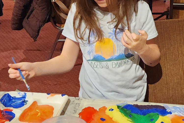 A child is using paint and a brush on a canvas, indicating a guided painting session or an open studio time.