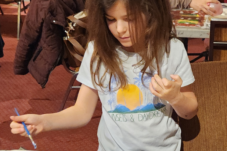 A child is using paint and a brush on a canvas, indicating a guided painting session or an open studio time.