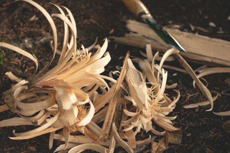 The image displays wood shavings, likely from a carving or whittling project, with a knife visible in the background