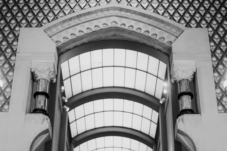a black and white photograph of interior space of the Historic Landmark Building, featuring a large, ornate arched window flanked by decorative, multi-bulb lamp posts. 