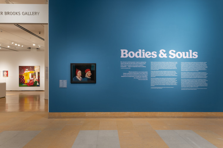 A blue museum gallery wall features the bold title "Bodies & Souls" alongside an exhibition text panel and a framed double portrait of two figures