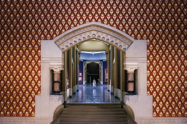 The image appears to show an interior hallway with patterned red and gold walls and a stone archway at the historic Pennsylvania Academy of the Fine Arts building in Philadelphia, designed by architect Frank Furness.