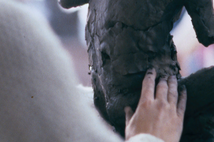 an artist working on a figurative clay sculpture in a studio setting, gently touching and shaping the dark, textured torso. 