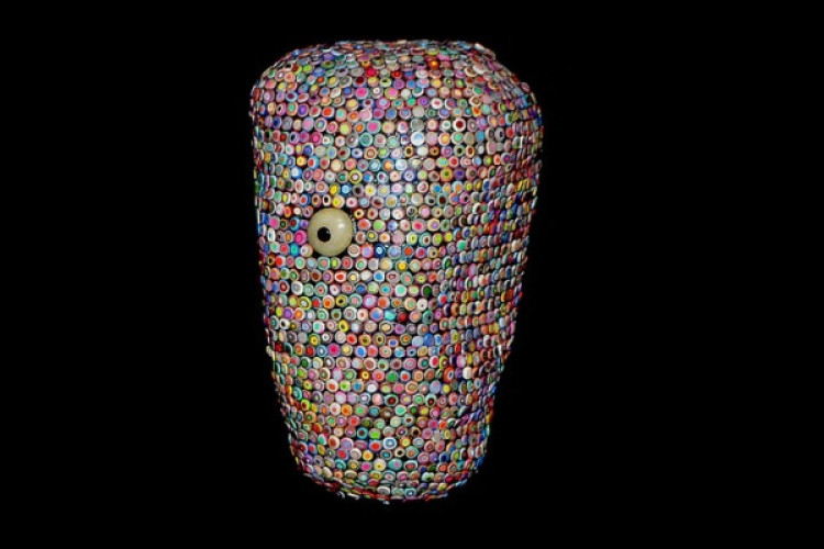  Mixed-media bust intricately encrusted with dense layers of multi-colored bottle caps and buttons, featuring a prominent, singular off-center eye.